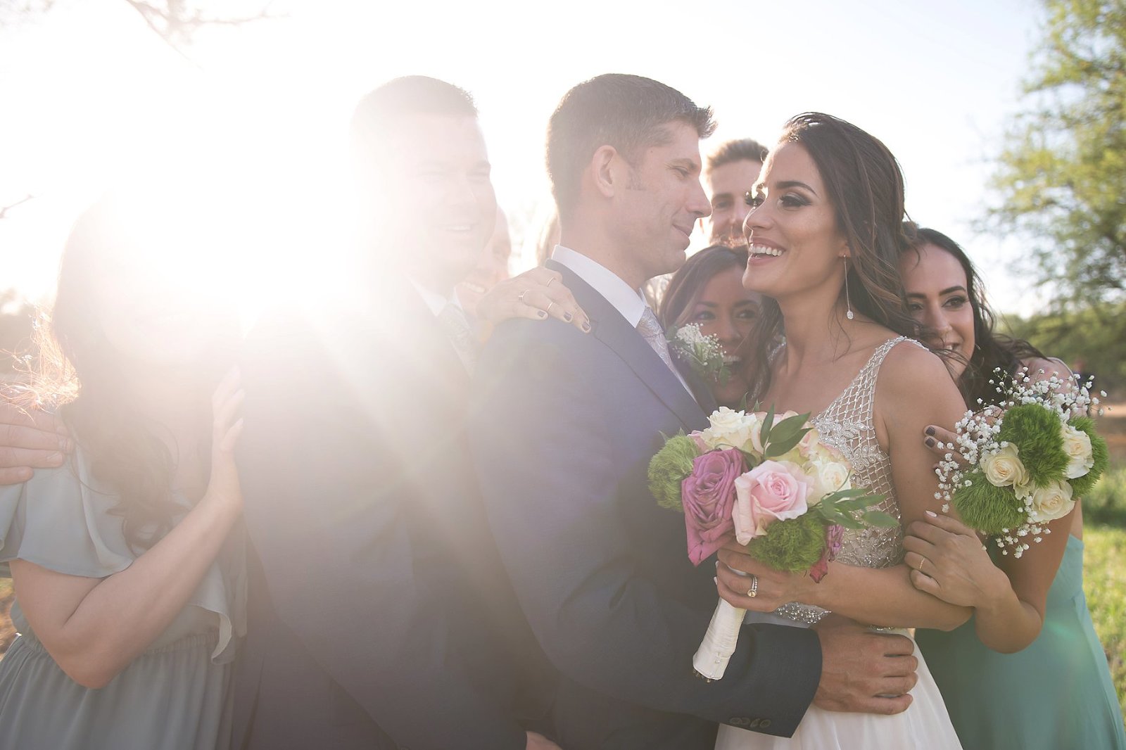 Bridal party hugging bride and groom after ceremony with lens flare